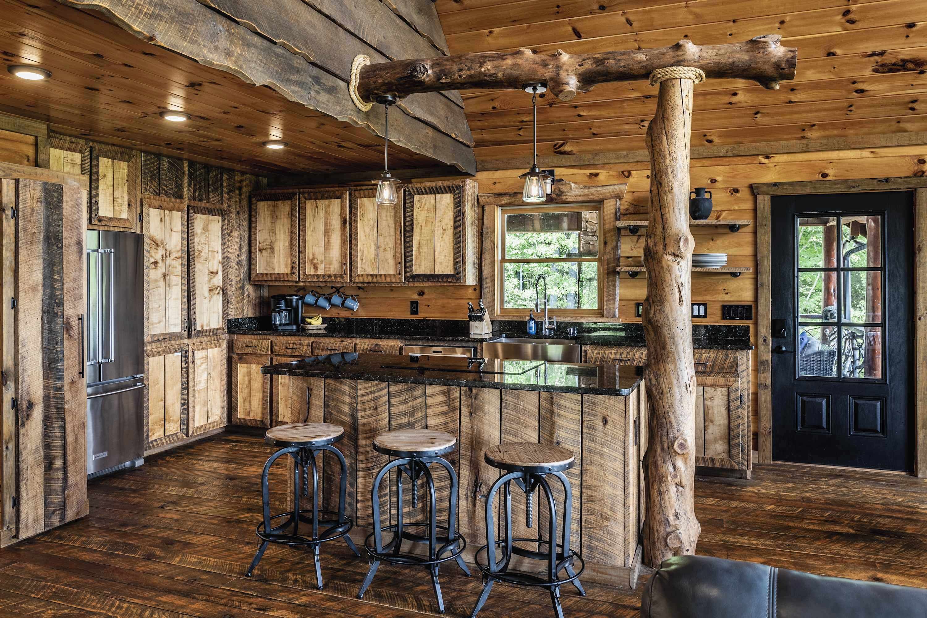 A rustic kitchen with wooden cabinets, a stainless steel refrigerator, a bar area with stools, and a large wooden beam ceiling.