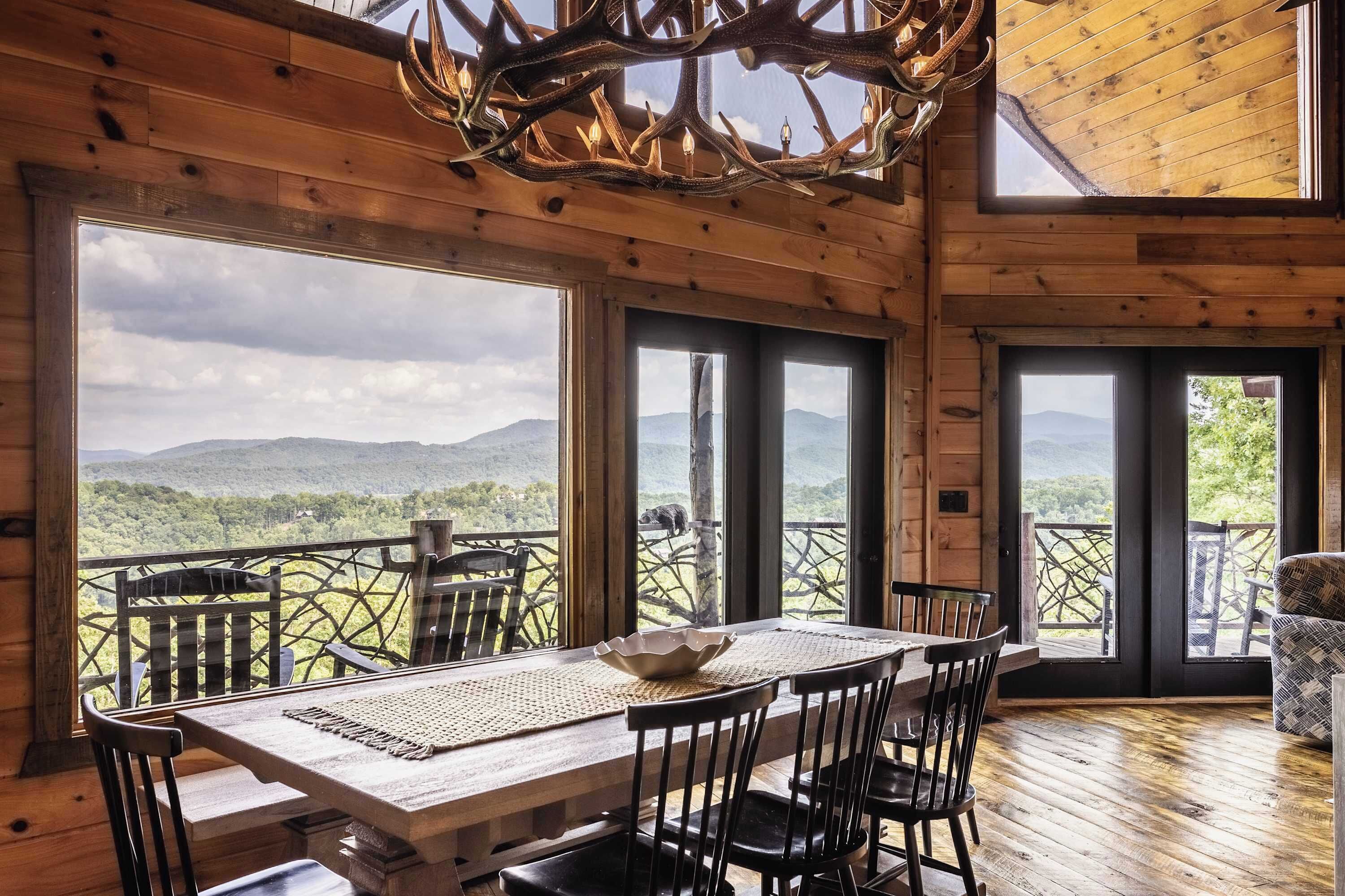 A wooden interior with a dining table and chairs, large windows offering a view of the outdoors.