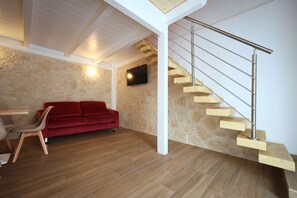 A modern living room with a red sofa, a wooden chair, a TV mounted on the wall, and a wooden staircase with a metal railing. - Hostmate - Bari - Garruba  (Bari)