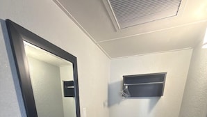 A bathroom with a mirror, a shelf, and a shower area.