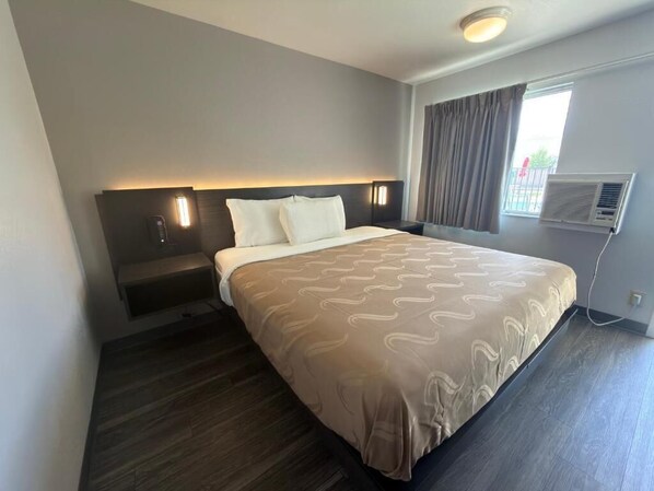 A hotel room with a bed, bedside tables, a wall-mounted air conditioner, and a window with curtains.