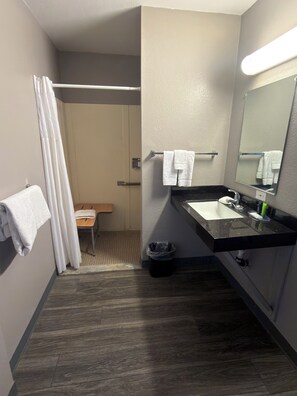 A hotel bathroom with a shower, a sink, a mirror, and a towel rack.