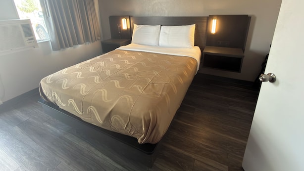 A hotel room with a bed, bedside tables, a window with curtains, and a door.