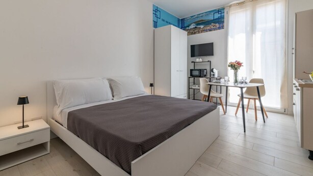 Un dormitorio moderno con cama, mesita de noche y un espacio de escritorio con silla.