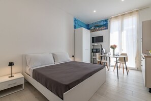 A modern bedroom with a bed, bedside table, and a desk area with a chair. - GuestHost - Casa Perni - The Sky Blue Room (Palermo)