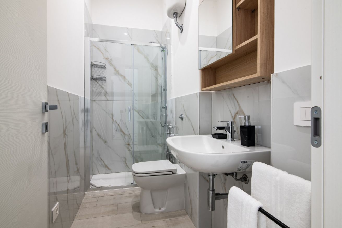 Een moderne badkamer met een douchecabine van glas, een wit wastafel en een houten opbergmeubel.