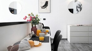 Ein moderner Essbereich mit einem langen Tisch, Stühlen, einer Blumenvase, einer Kaffeemaschine und Frühstücksgebäck.
