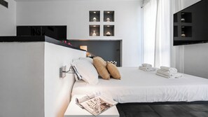 Ein modernes Hotelzimmer mit einem Bett, einem Nachttisch mit einer Zeitschrift, einer Wandlampe und einem Fernseher.