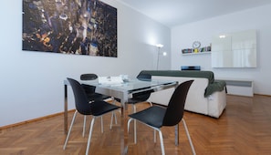 A modern living room with a glass dining table, black chairs, a white sofa, and a large cityscape painting on the wall. - Italianway Easy - De Cristoforis 12 A (Milan)