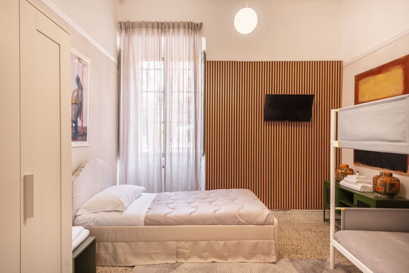 Ein Schlafzimmer mit einem Bett, einem an der Wand befestigten Fernseher, einem Etagenbett und einem Fenster mit Vorhängen.