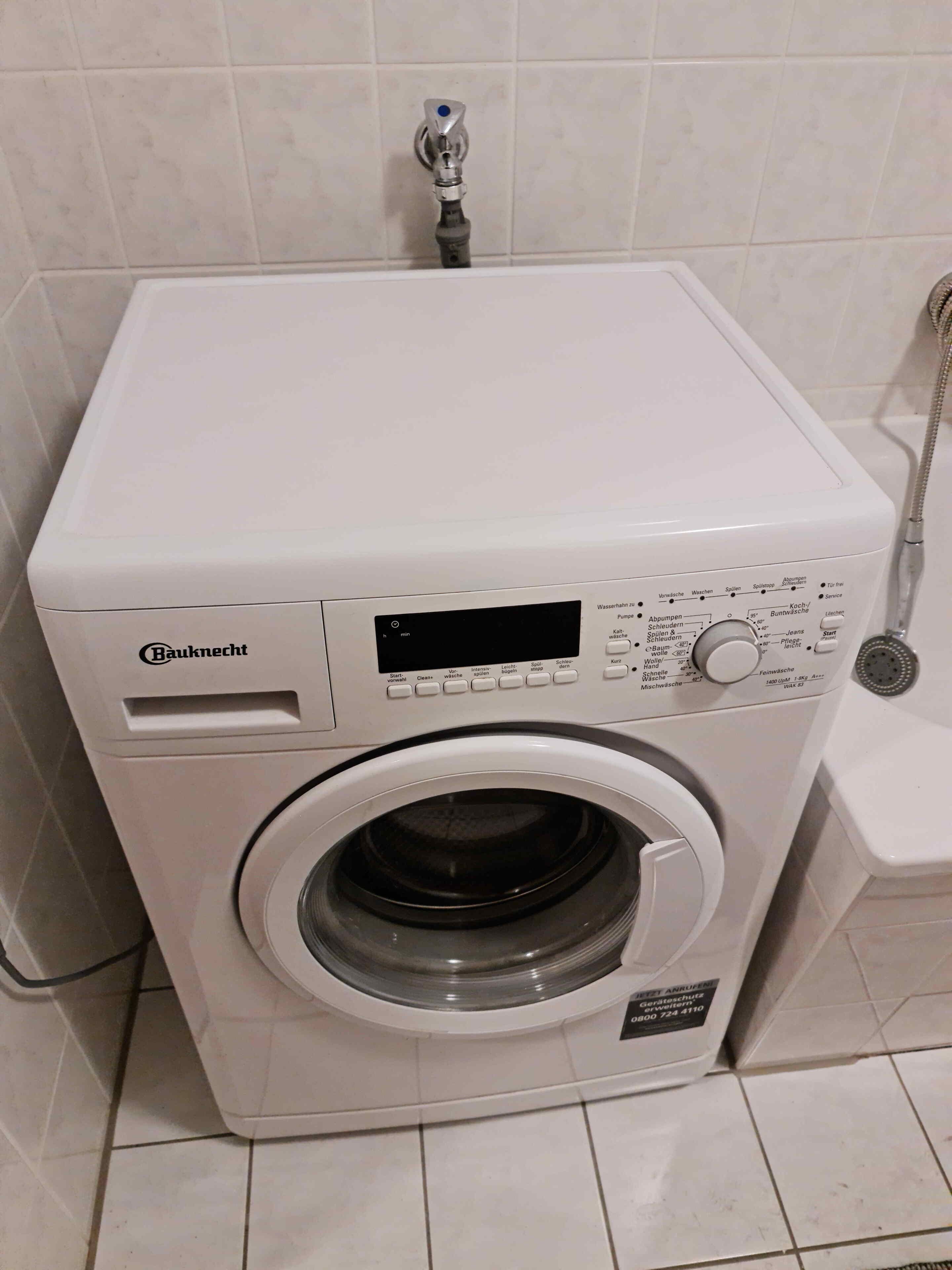 Eine Bauknecht Waschmaschine mit Frontlader in einem Badezimmer mit Fliesenboden und einer Duschbrause.