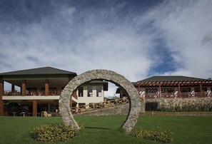 A stone archway in a well-maintained lawn area with a building featuring a balcony and a covered patio in the background.