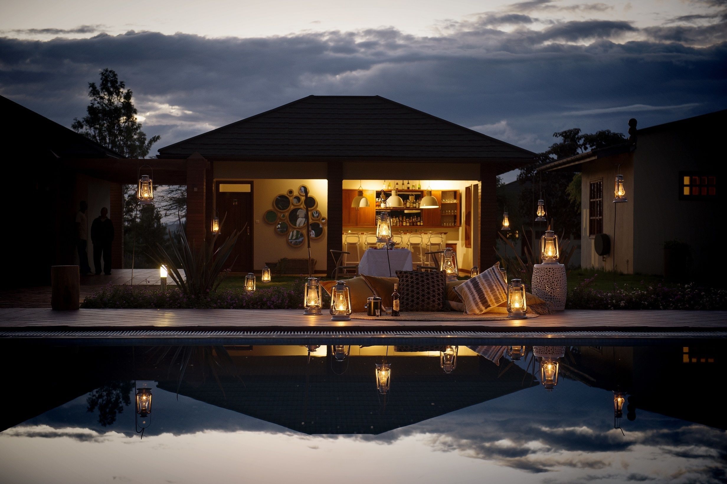 Ein Haus mit Pool im Vordergrund, eine überdachte Sitzterrasse mit Tischen und Stühlen sowie eine Bar, die durch die offene Vorderseite sichtbar ist.