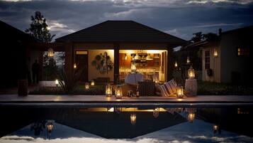 Ein Haus mit Pool im Vordergrund, eine überdachte Sitzterrasse mit Tischen und Stühlen sowie eine Bar, die durch die offene Vorderseite sichtbar ist.