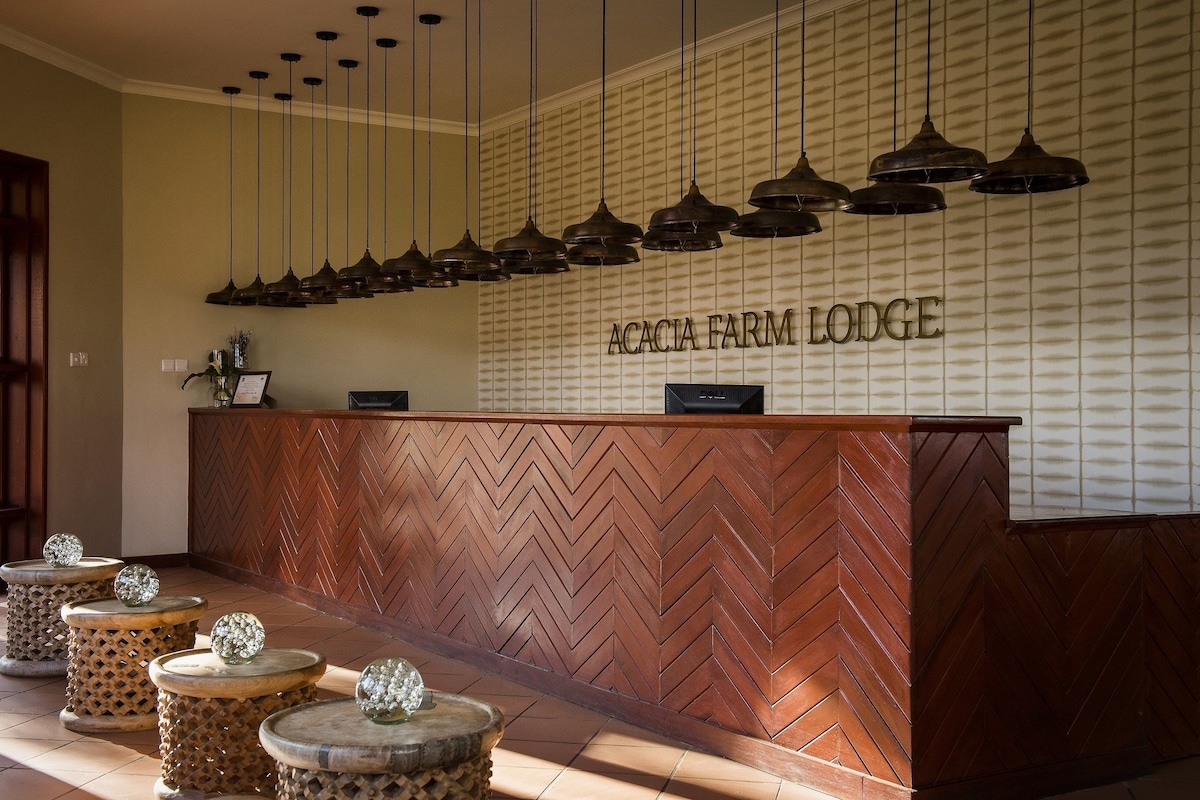 A reception desk with a herringbone wood pattern, a sign reading 'ACACIA FARM LODGE', and multiple pendant lights above.