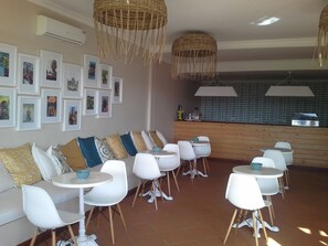 Un comedor con sillas y mesas blancas, un banco de madera y cuadros en la pared.