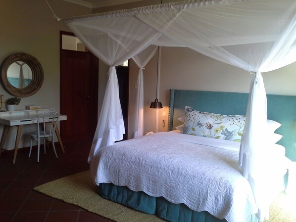Un dormitorio con cama, escritorio, silla, lámpara de noche y espejo en la pared.