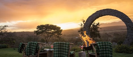 An outdoor seating area with chairs and tables, a stone archway, and a fire.