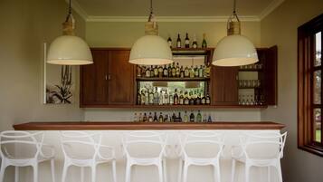 A bar area with a wooden countertop, multiple bottles, and white plastic chairs.