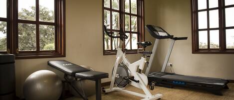 A home gym with a stationary bike, treadmill, exercise ball, and bench.