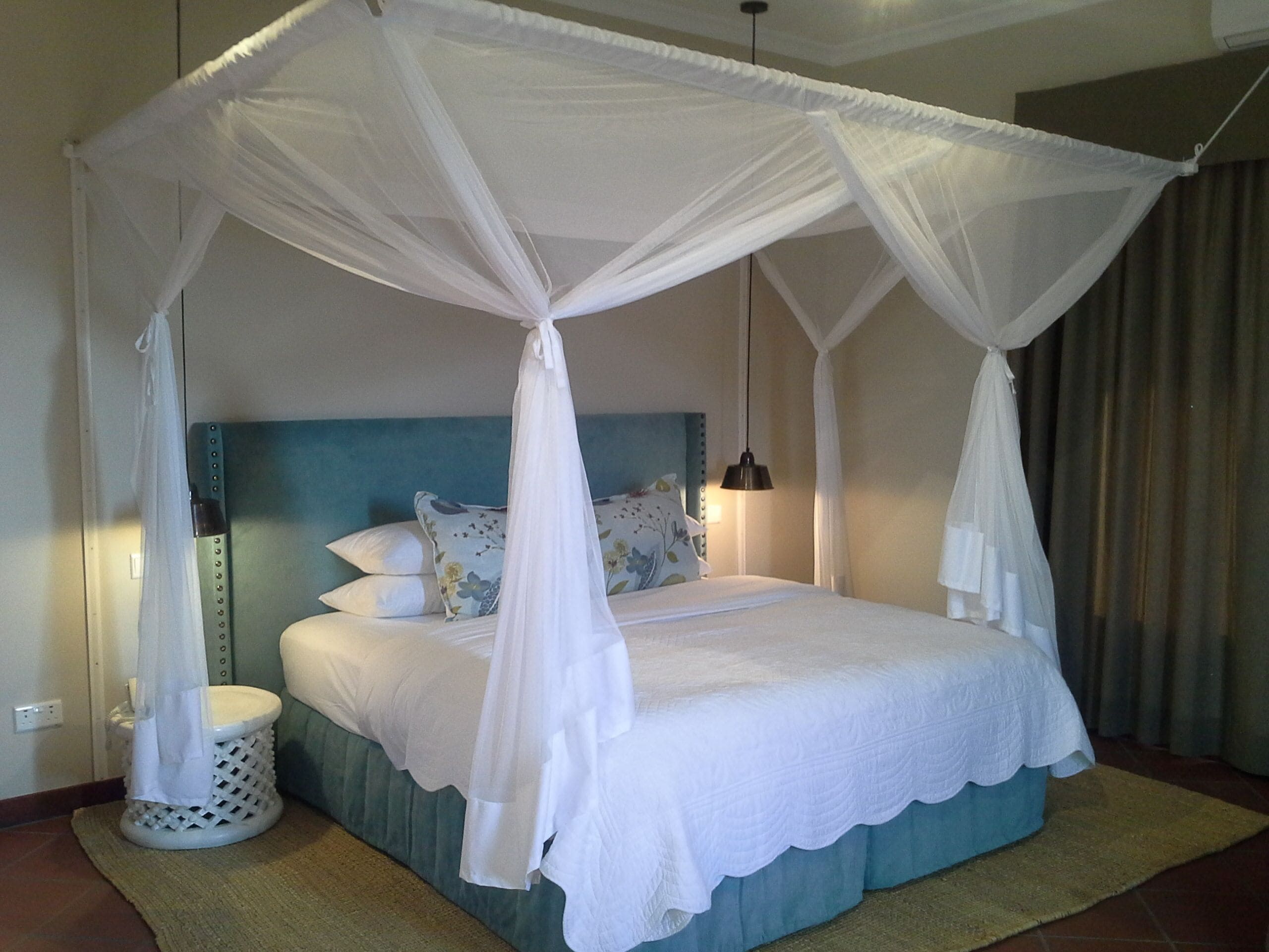 A four-poster canopy bed with a headboard, pillows, and a bedside lamp.