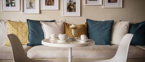 A modern living room with a sofa, two chairs, a coffee table, and a tray with cups and a dessert.