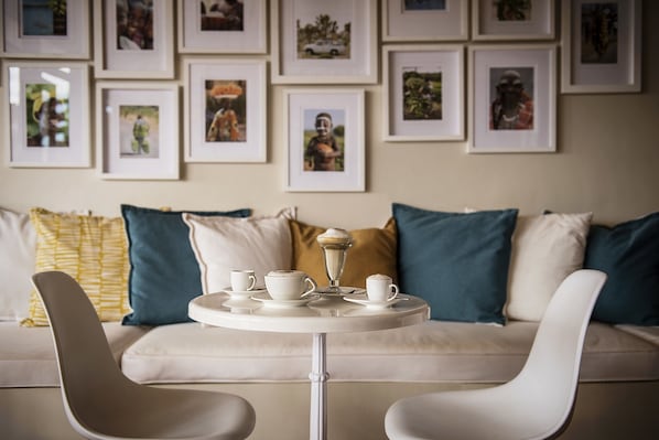 A modern living room with a sofa, two chairs, a coffee table, and a tray with cups and a dessert. - Acacia Farm Lodge (Karatu)