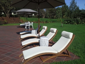 A patio with sun loungers, a table, and chairs under a large umbrella.