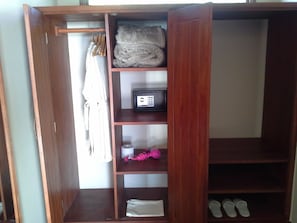 A wooden wardrobe with multiple shelves, a hanging rack, and a folded towel. - Acacia Farm Lodge (Karatu)