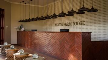 Ein Empfangsschalter mit Fischgrätparkett, ein Schild mit der Aufschrift 'ACACIA FARM LODGE' und mehrere Pendelleuchten darüber.