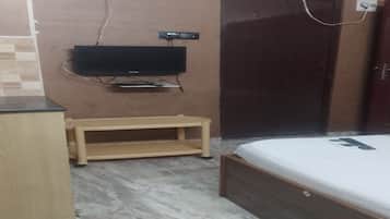 A bedroom with a bed, a television mounted on the wall, a wooden bench, and a wardrobe.