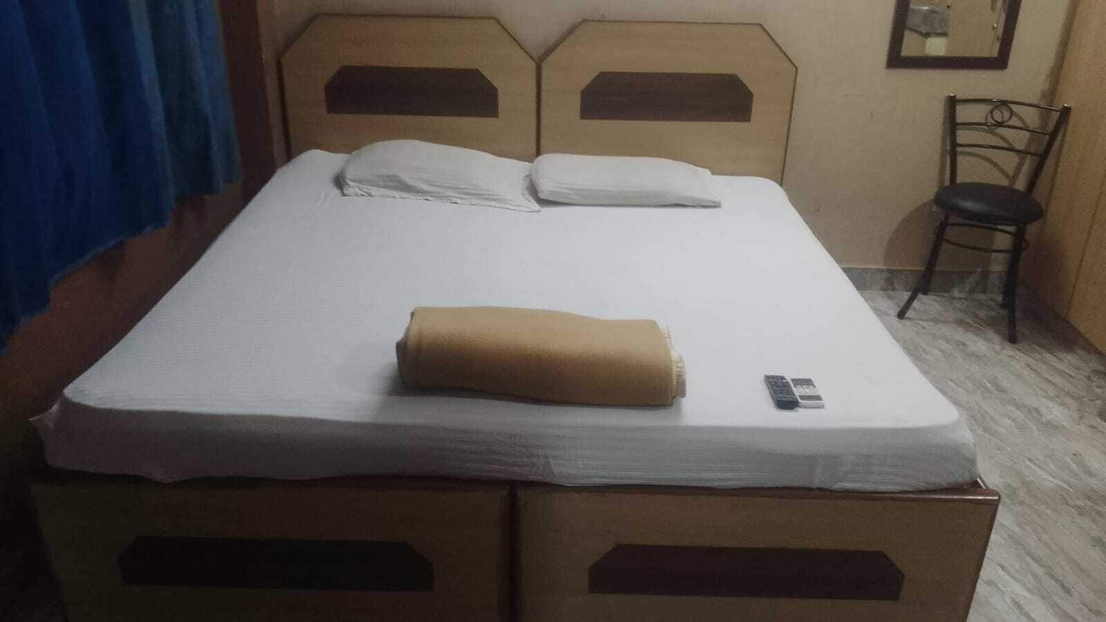 Una cama individual con un colchón blanco y dos almohadas, una toalla enrollada y un control remoto sobre la cama.
