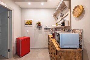 Eine kleine Küche mit einem roten Kühlschrank, einer Mikrowelle auf einem Holzschrank und einer Wanduhr.