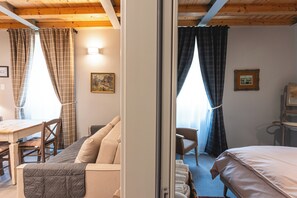 Ein Zimmer mit einem Bett, einem Schreibtisch, einem Stuhl und einem Sofa. Vor den Fenstern hängen Vorhänge, und an der Wand hängt ein Gemälde.