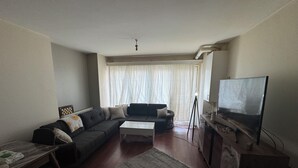 A living room with a sofa, a coffee table, a television, and a window with curtains. - Beautiful 1-bedroom apartment in tranquil İstanbul neighborhood (İstanbul)