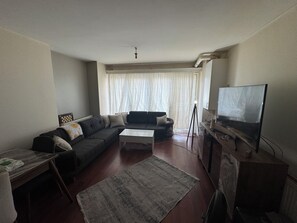 A living room with a sofa, a coffee table, a television, and a window with curtains. - Beautiful 1-bedroom apartment in tranquil İstanbul neighborhood (İstanbul)