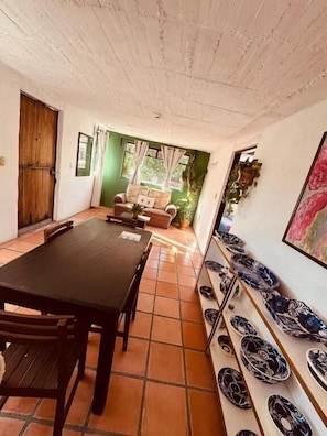 Una habitación con una mesa y sillas de madera, un sofá, una pared verde y una estantería con platos decorativos.