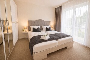 A double bed with a tufted headboard, bedside tables with lamps, a large window with sheer curtains, and a wardrobe with mirrored doors. - Vrbo Property (Sellin)