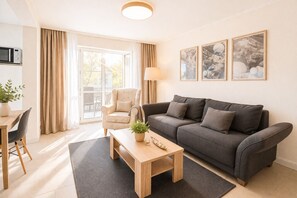 A modern living room with a sofa, a coffee table, a chair, and a lamp. There is a window with curtains, a plant, and framed pictures on the wall. - Villa Manatee - Wellness Apartment with a Balcony (Sellin)