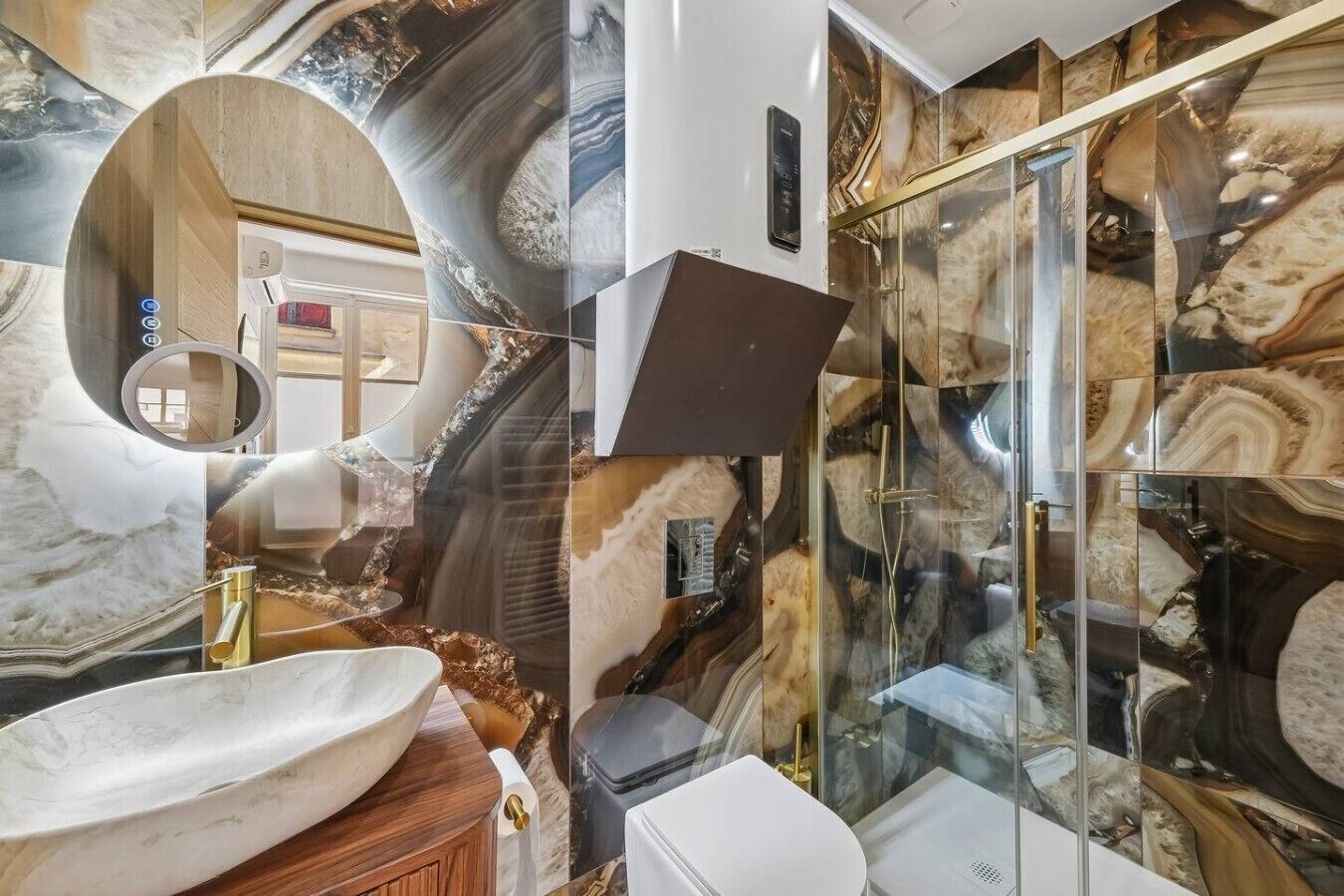 A bathroom with a large oval sink, a glass shower enclosure, and marble-like wall tiles.