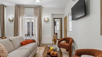 A modern living room with a sofa, armchair, coffee table, and a flat-screen TV mounted on the wall.
