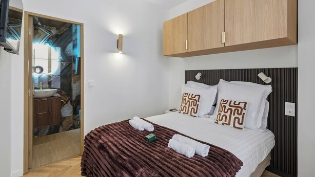 A modern bedroom with a bed, wooden wardrobe, and a bathroom with a mirror and sink. - Lavie Maison - Spa Bath & AC, Heart of Saint-Merri (Paris)