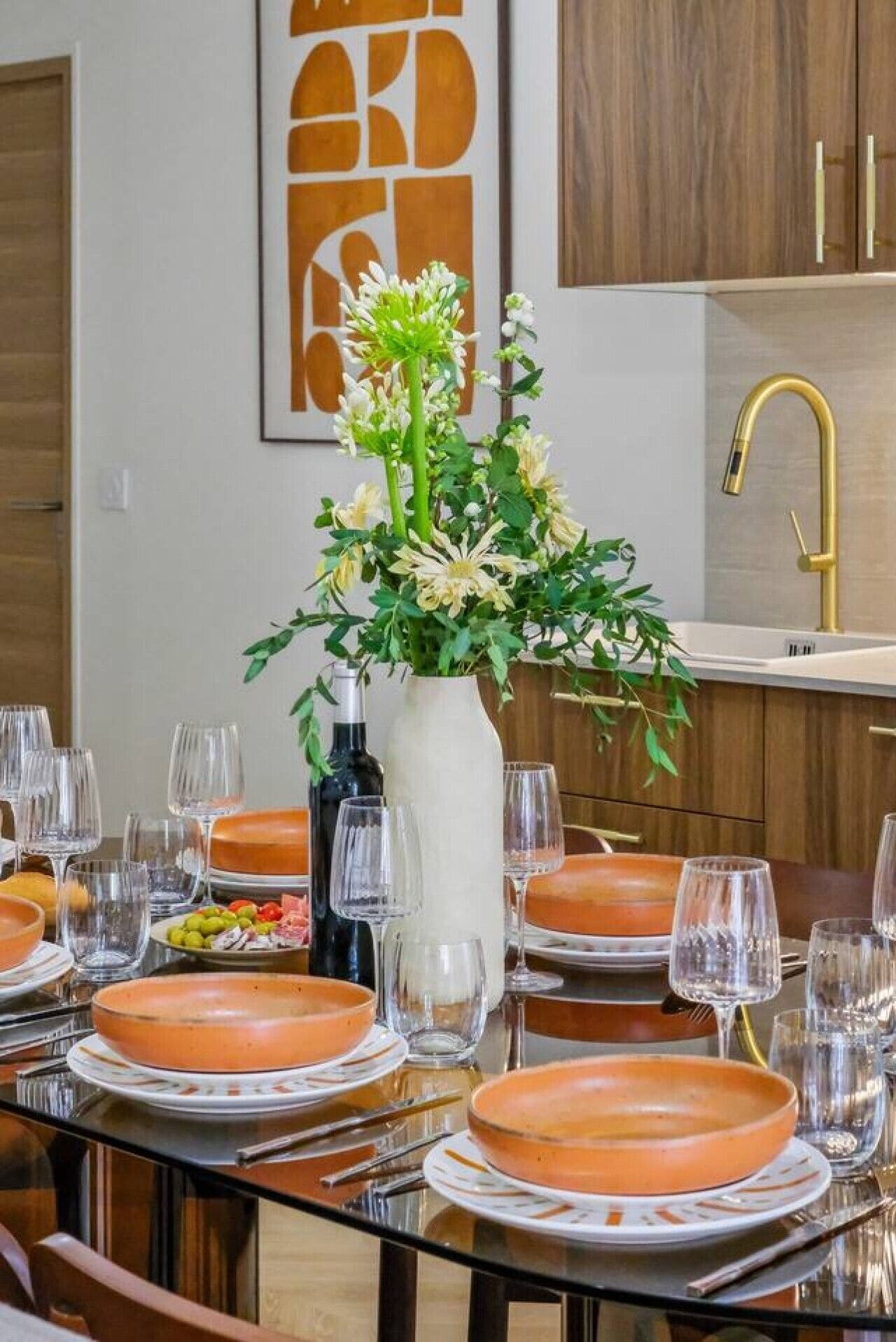 A dining table set with plates, glasses, and cutlery, a vase with flowers, and a bottle of wine.