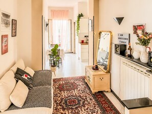 A living room with a sofa, a coffee table, a rug, a mirror, and a kitchen area in the background. - Jo's Terrace - Centocelle (Roma)