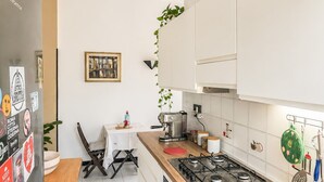 A modern kitchen with white cabinets, a gas stove, and a dining area with a table and chairs. - Jo's Terrace - Centocelle (Roma)