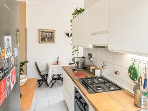 A modern kitchen with white cabinets, a gas stove, and a dining area with a table and chairs. - Jo's Terrace - Centocelle (Roma)