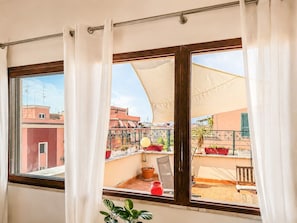 A balcony with a view of neighboring buildings, a chair, a table, and a potted plant. - Jo's Terrace - Centocelle (Roma)