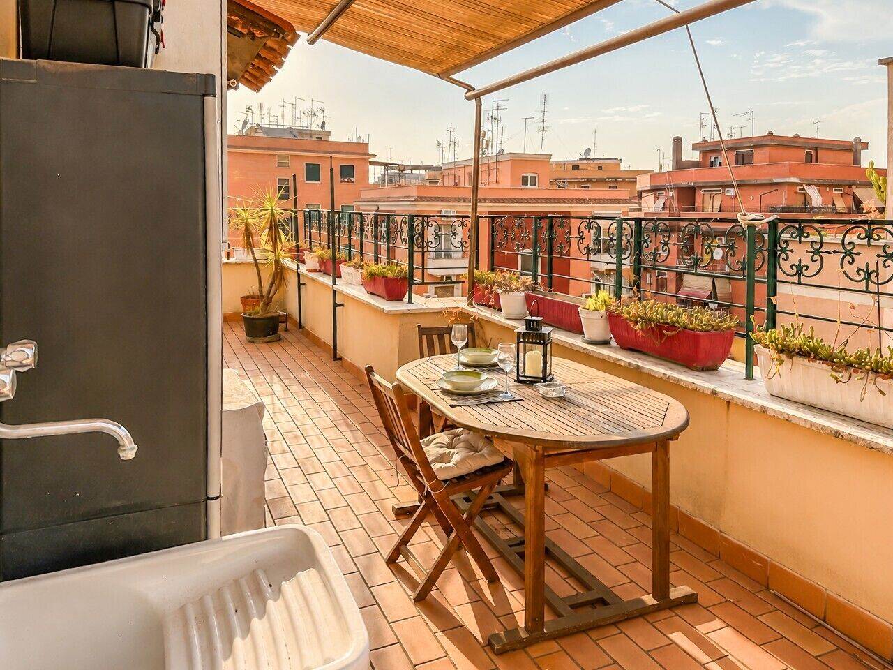 A rooftop terrace with a table and chairs, potted plants, and a view of surrounding buildings.