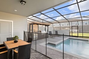 Un patio moderno al aire libre con cerramiento de vidrio, una piscina y un área de comedor con sillas y una mesa.