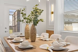 A dining area with a long table set for a meal, two large vases with greenery, and a window with blinds. - 5 Bd / 4.5 Ba / Sleeps 14 / Windsor Cay Resort (Clermont)